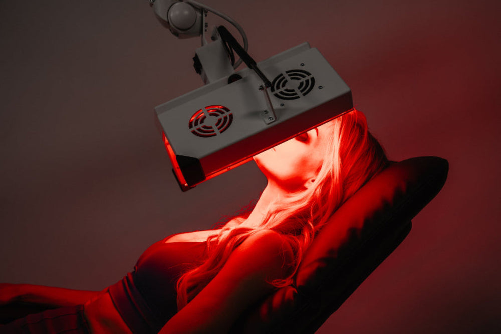 Person receiving red light therapy under a device with a dark background