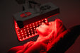 Person receiving red light therapy treatment with a device.