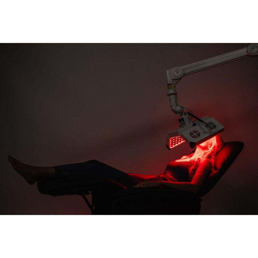 Person receiving red light therapy under a medical device with a dark background