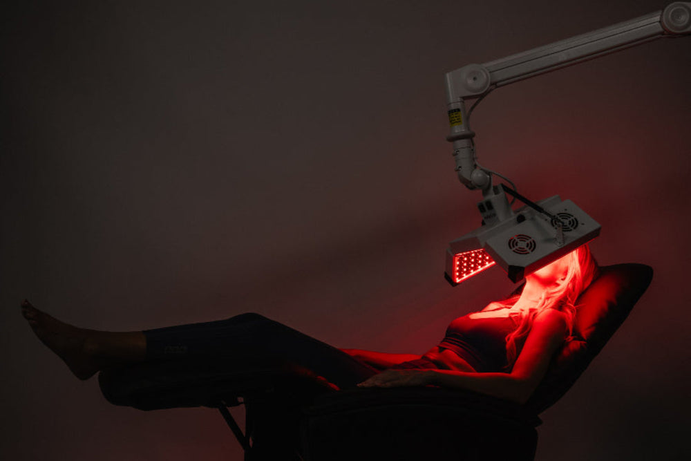 Person receiving red light therapy under a medical device with a dark background