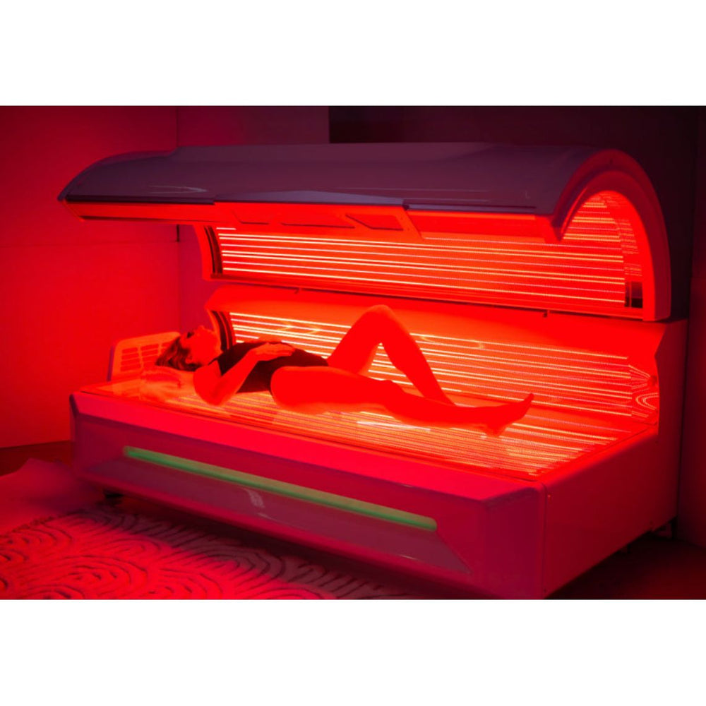 Woman lying inside a red light therapy bed, the bed is turned on