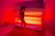 Person standing in front of a red light therapy machine in a dimly lit room.
