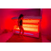Person standing in front of a red light therapy machine in a dimly lit room.