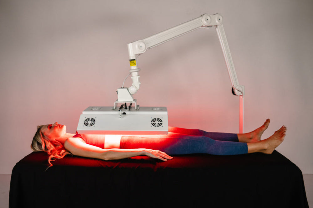 Person receiving red light therapy on a black table with a neutral background