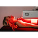 Person receiving red light therapy with a machine on a pink background
