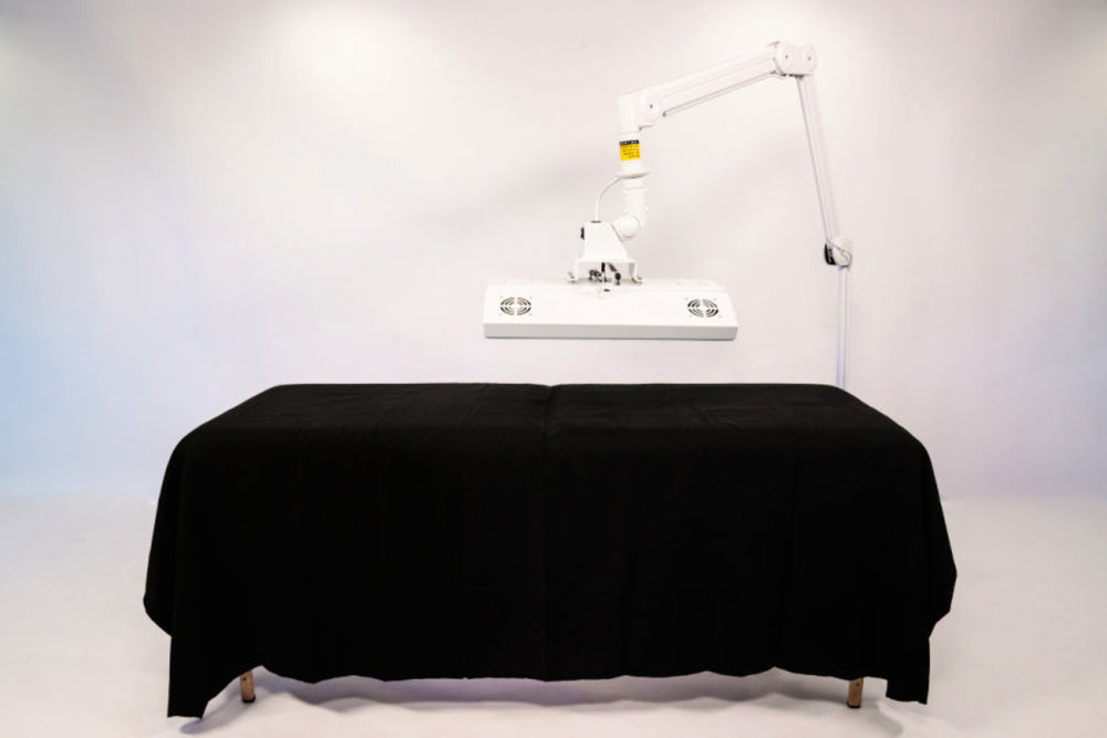 Massage table with black cover and overhead lighting on a white background