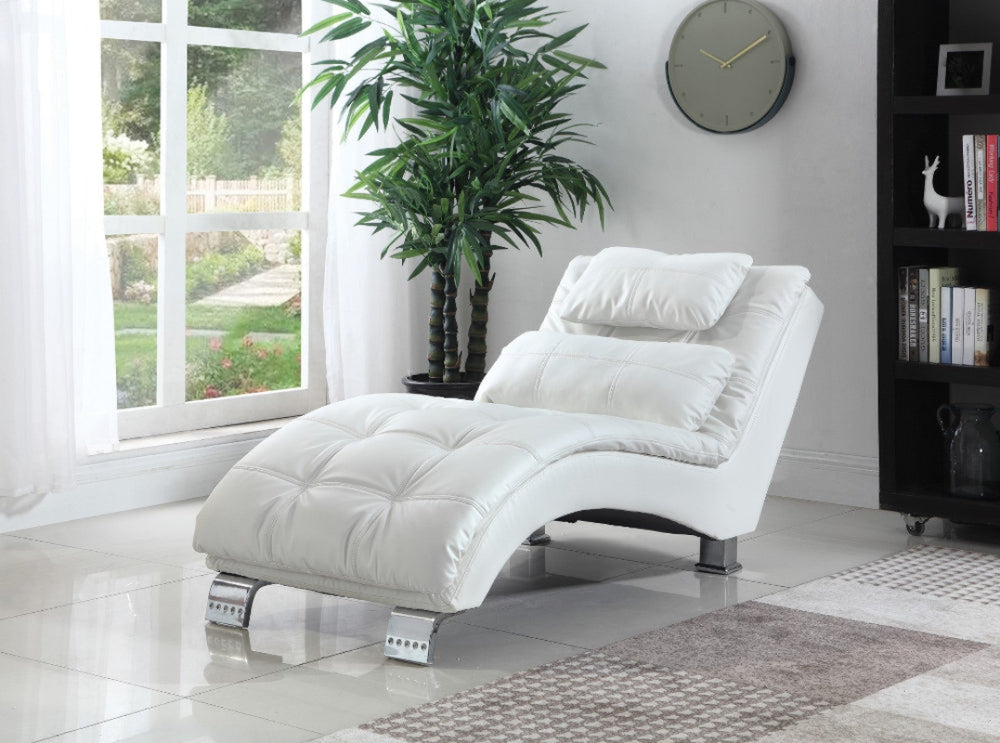 White chaise lounge chair in a room with a large window, plant, and bookshelf.