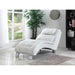 White chaise lounge chair in a room with a large window, plant, and bookshelf.