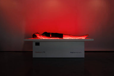 Person lying on a white platform with red lighting in a dark room