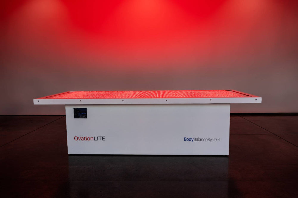 White device labeled 'OvationLITE' with red light on a dark floor against a red wall.