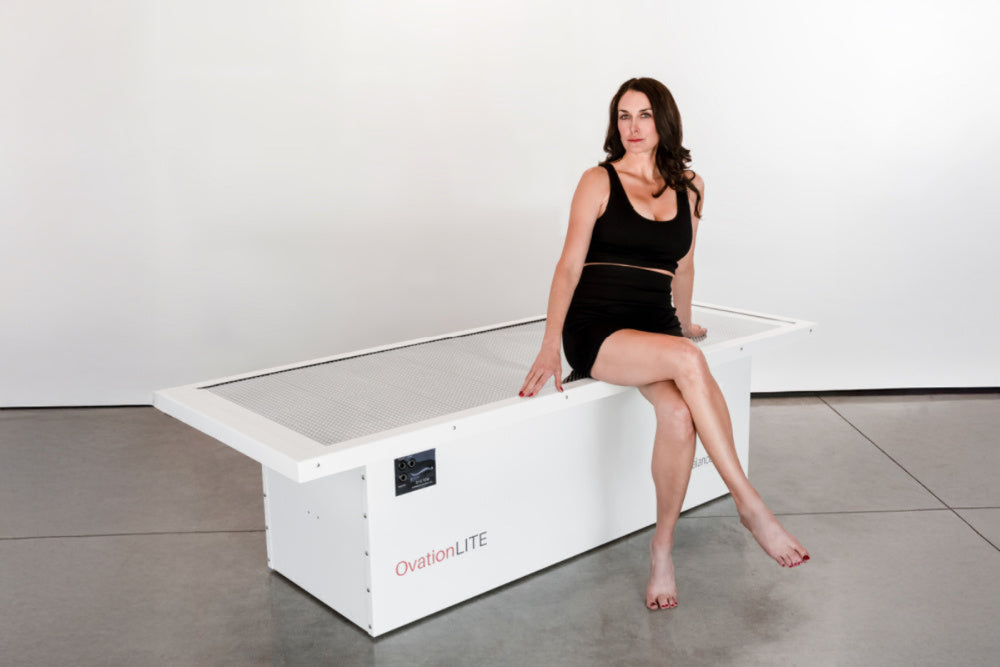 Woman sitting on a white exercise machine with 'OvalFit' branding against a white background