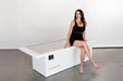 Woman sitting on a white exercise machine with 'OvalFit' branding against a white background