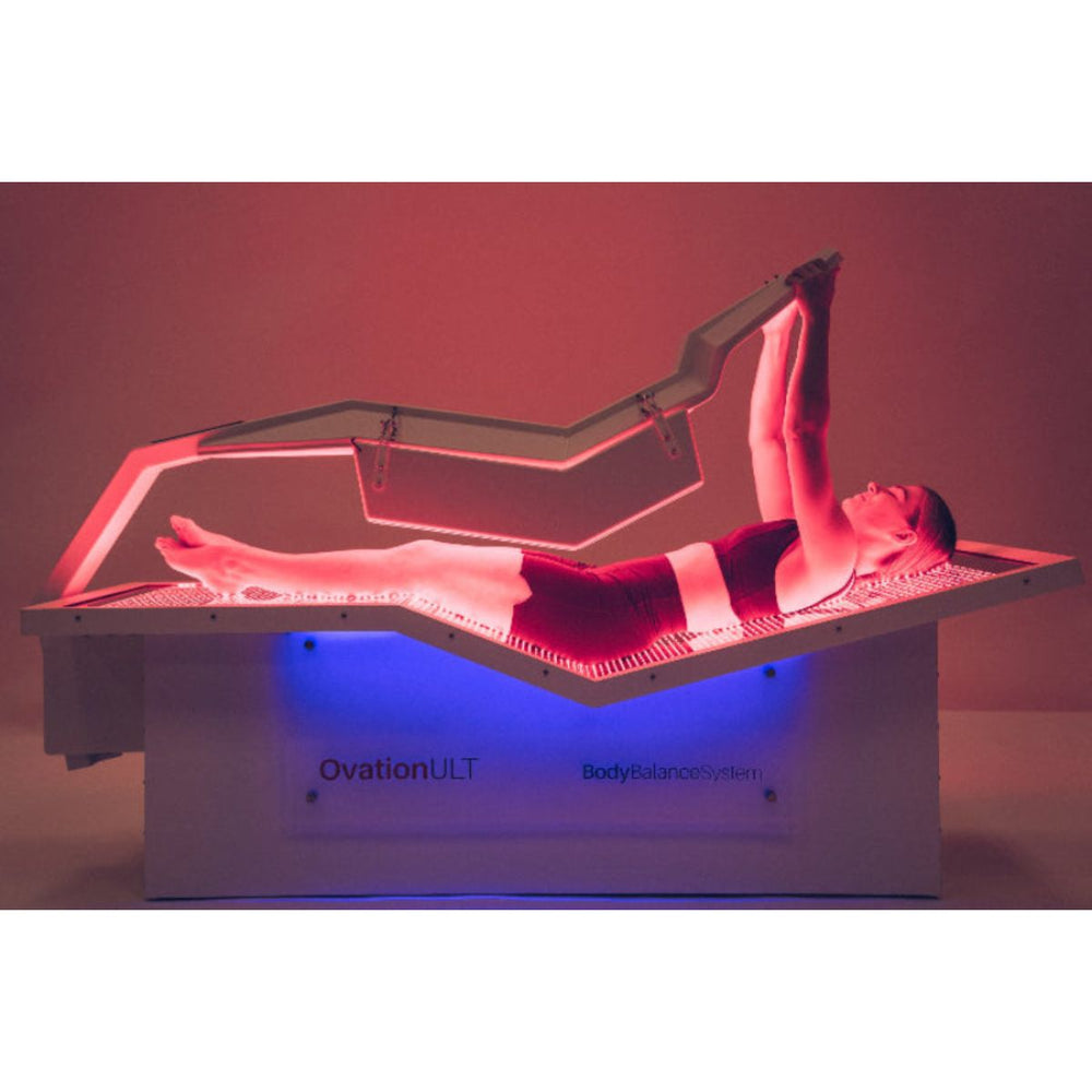 Person lying on a medical device labeled 'OvationULT' with red and blue lighting.