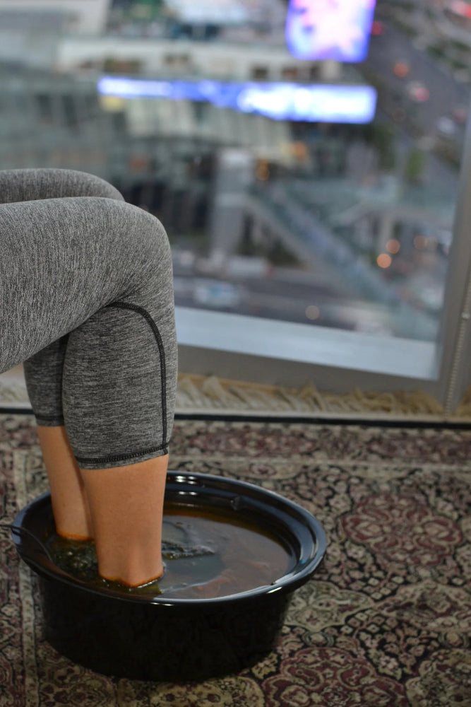 Person sitting with feet in a bowl of water on a patterned rug with a cityscape in the background