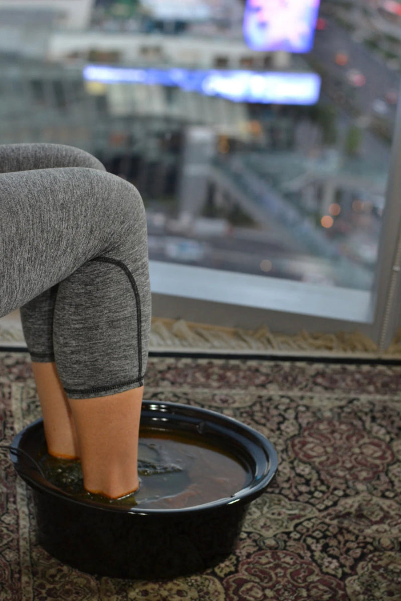 Person sitting with feet in a bowl of water on a patterned rug with a cityscape in the background