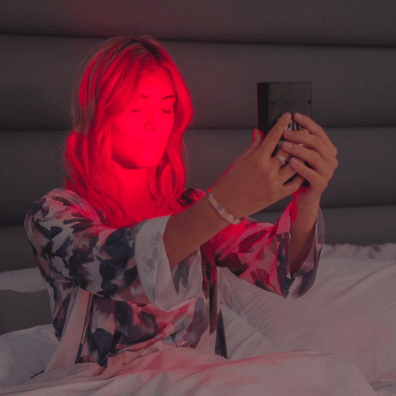 Person sitting on a bed using a phone with red lighting