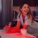 Woman sitting at a table with a red light-emitting device and a mug in a kitchen setting.