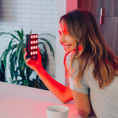 Woman holding a small, rectangular light device with multiple LED lights on a table.