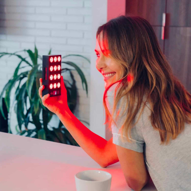 Woman holding a small, rectangular light device with multiple LED lights on a table.