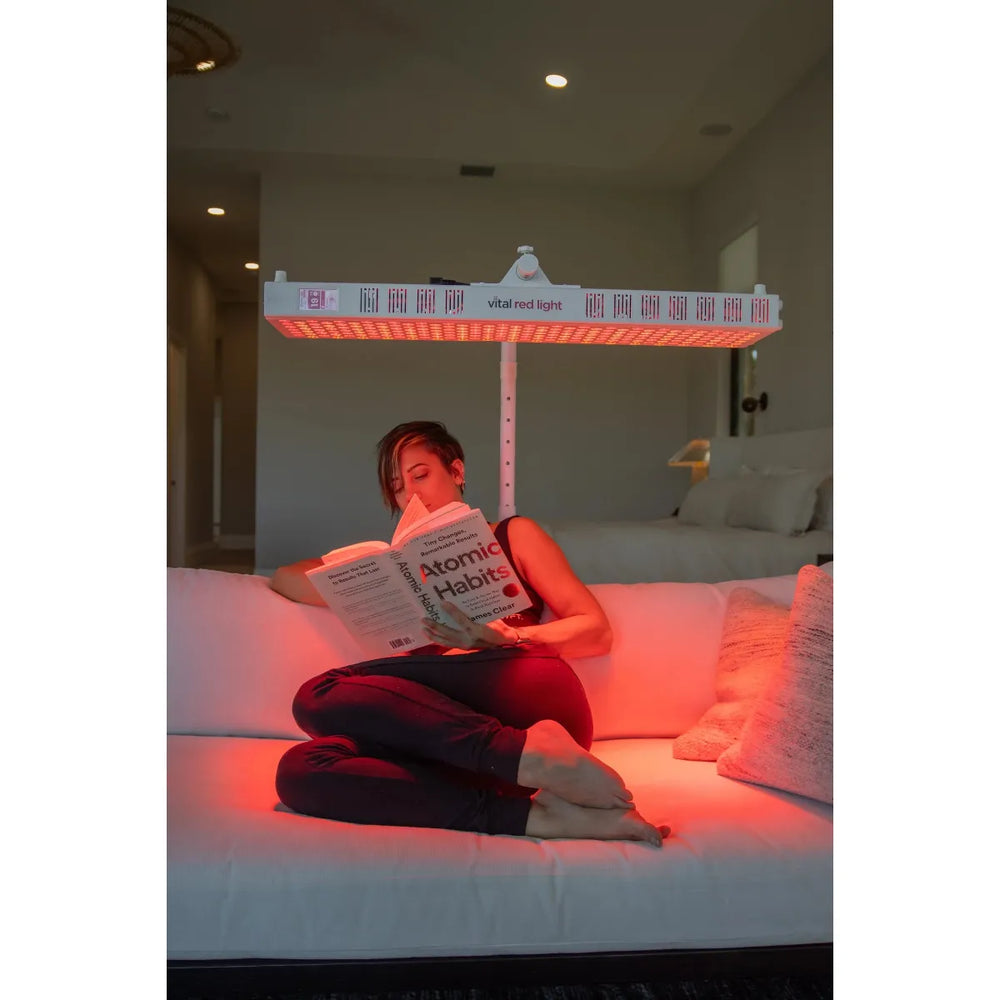 Person reading a book on a bed with a red light therapy lamp above them