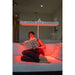 Person reading a book on a bed with a red light therapy lamp above them