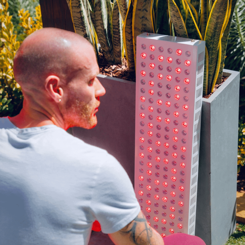 Man sitting next to a tall rectangular light fixture with red LED lights outdoors.