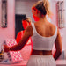 Woman in a white sports bra and shorts holding a pink LED light device in a room with red lighting.