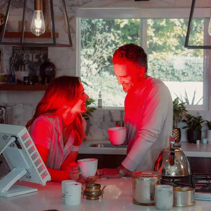 Two people in a kitchen with red lighting, sitting at a table with coffee cups.